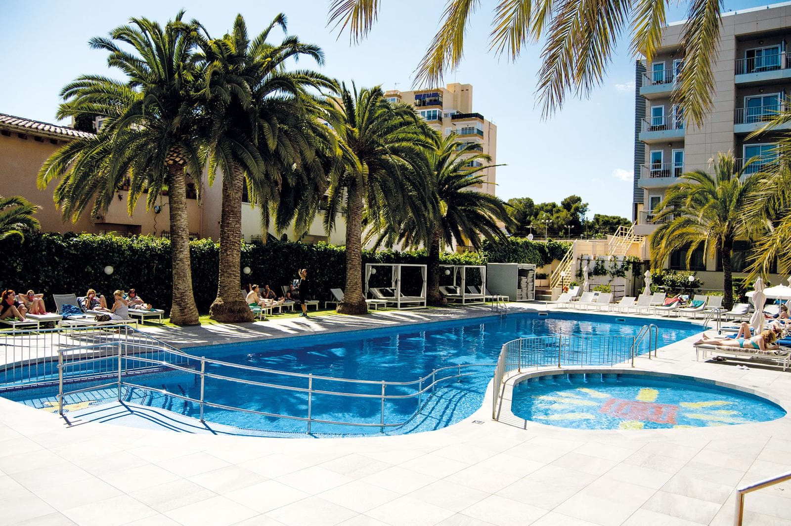 Hotelpool mit Palmen, Liegestühlen und modernem Ambiente unter sonnigem Himmel.
