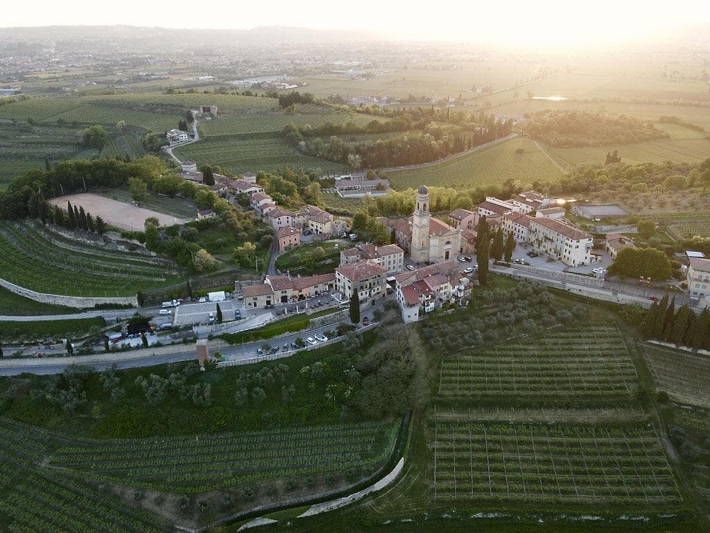 Luftaufnahme eines italienischen Dorfes bei Sonnenuntergang, umgeben von Weinbergen.