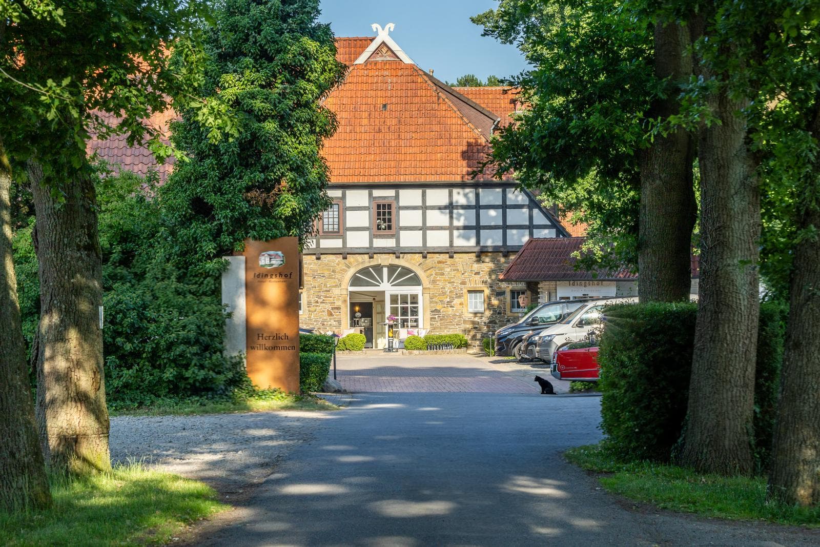 Fachwerkhotel mit roten Dächern, von Bäumen umgeben, sonnige Begrüßungsszene.
