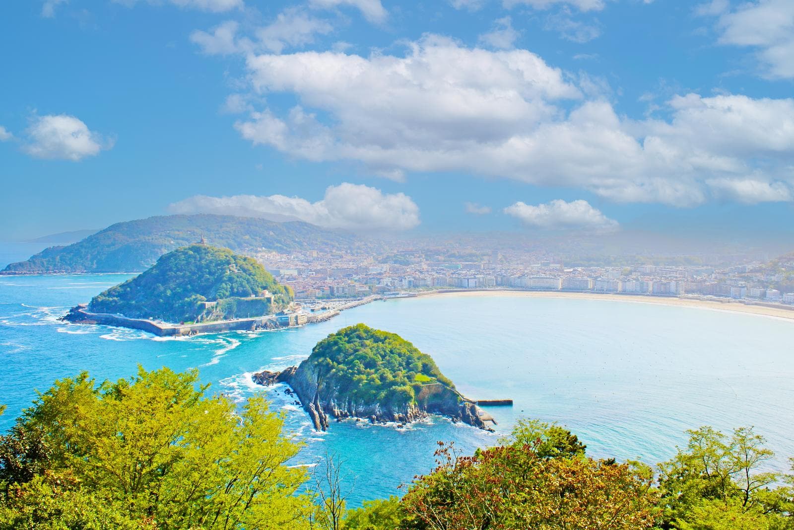 Küstenblick auf San Sebastián, Spanien, mit grünem Inselhügel und blauem Meer.