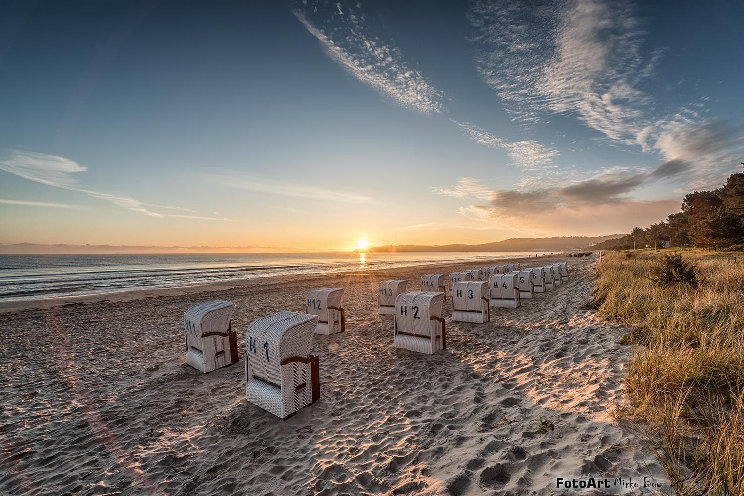 Sonnenaufgang am Ostseestrand mit Strandkörben und sanften Wellen.