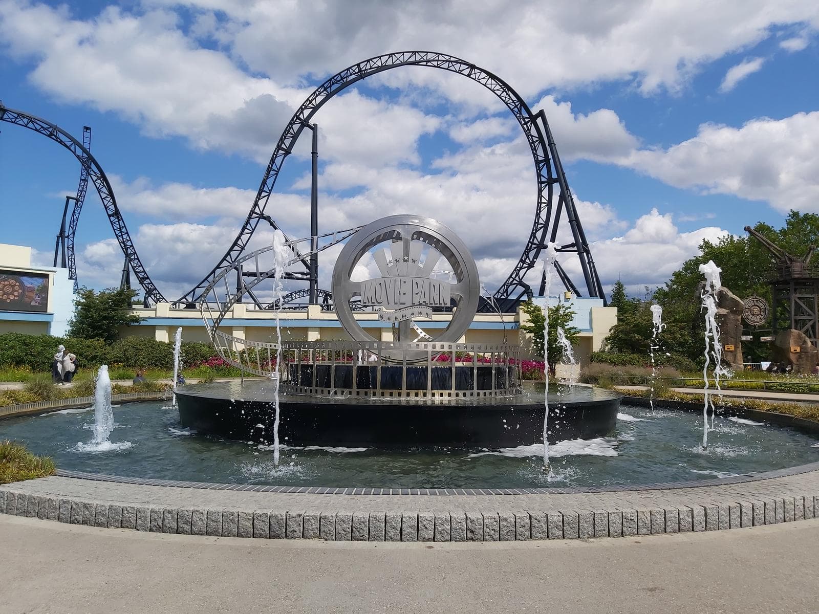 Achterbahn im Movie Park Germany mit sprudelndem Springbrunnen bei blauem Himmel.