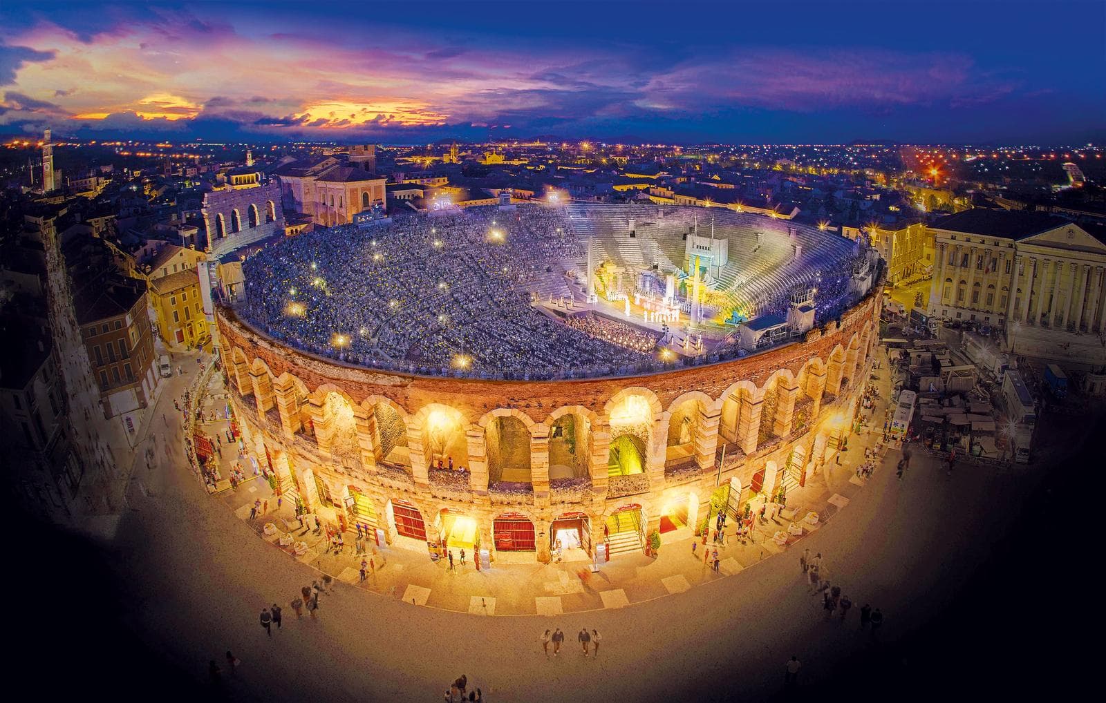 Belebte Arena bei Nacht in Verona, Italien, mit beeindruckendem Sonnuntergang im Hintergrund.