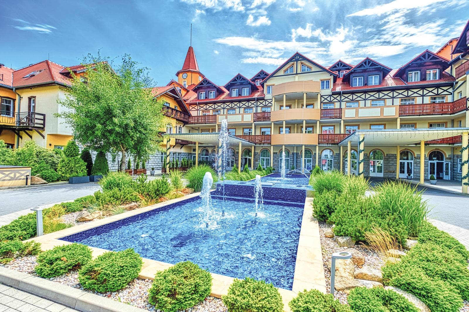 Charmantes Hotel mit rotem Dach, Fachwerkstil, Brunnen und gepflegtem Garten.