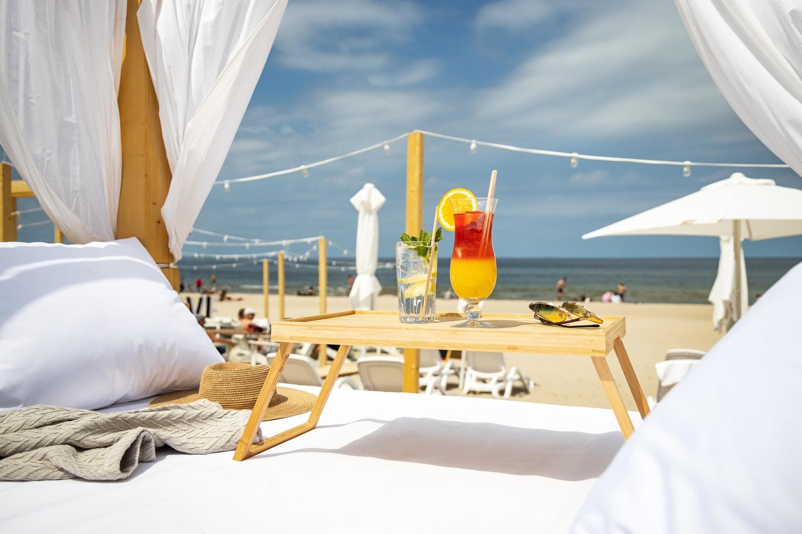 Luxuriöses Strandbett mit Cocktails, weißem Sonnenschirm und entspannter Urlaubsatmosphäre.