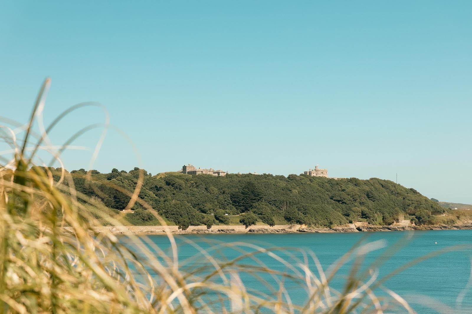 Küste mit grüner Hügellandschaft und Burgen in weiter Ferne unter klarem Himmel.