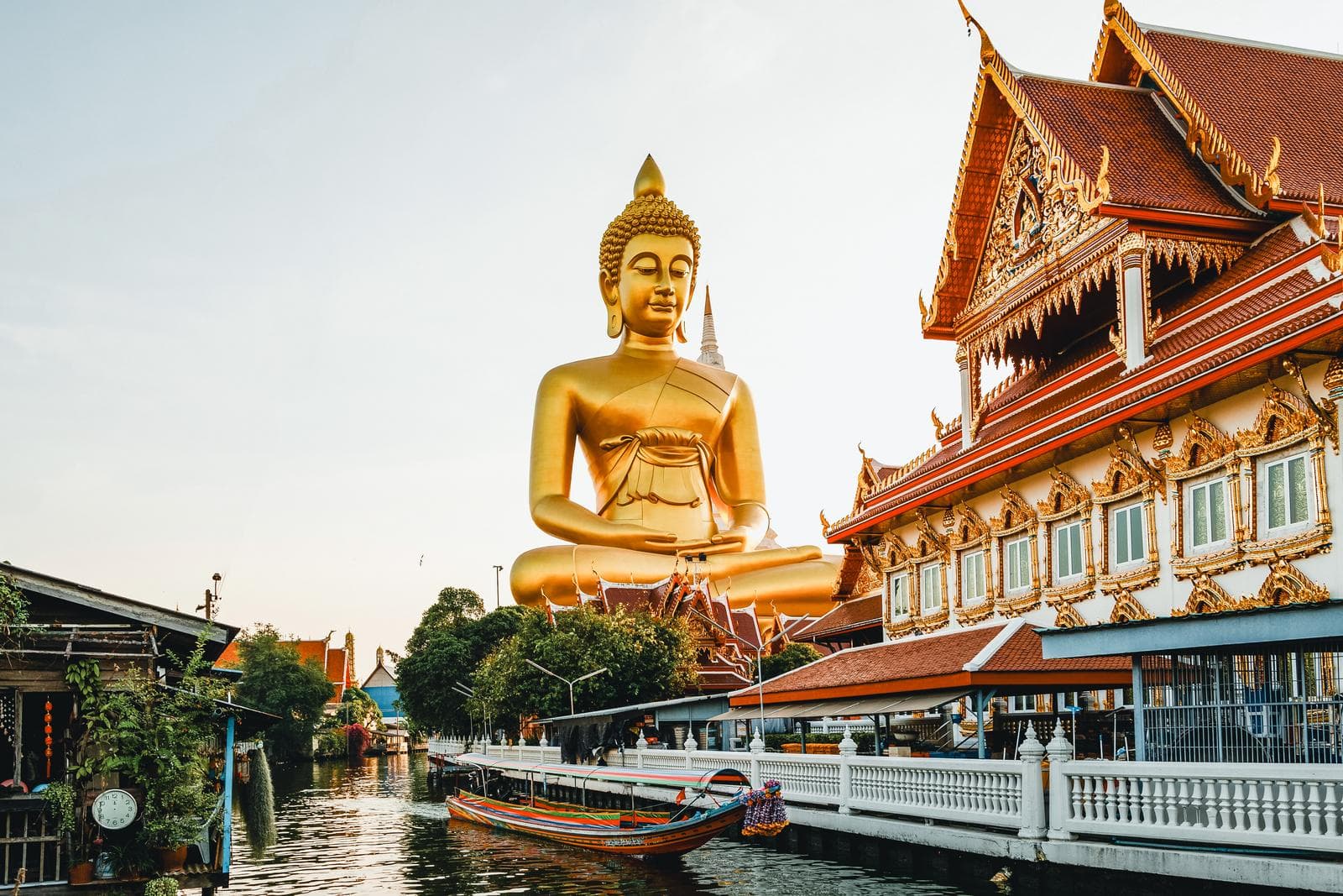 Goldene Buddha-Statue und prachtvoller Tempel in Thailand am Flussufer.