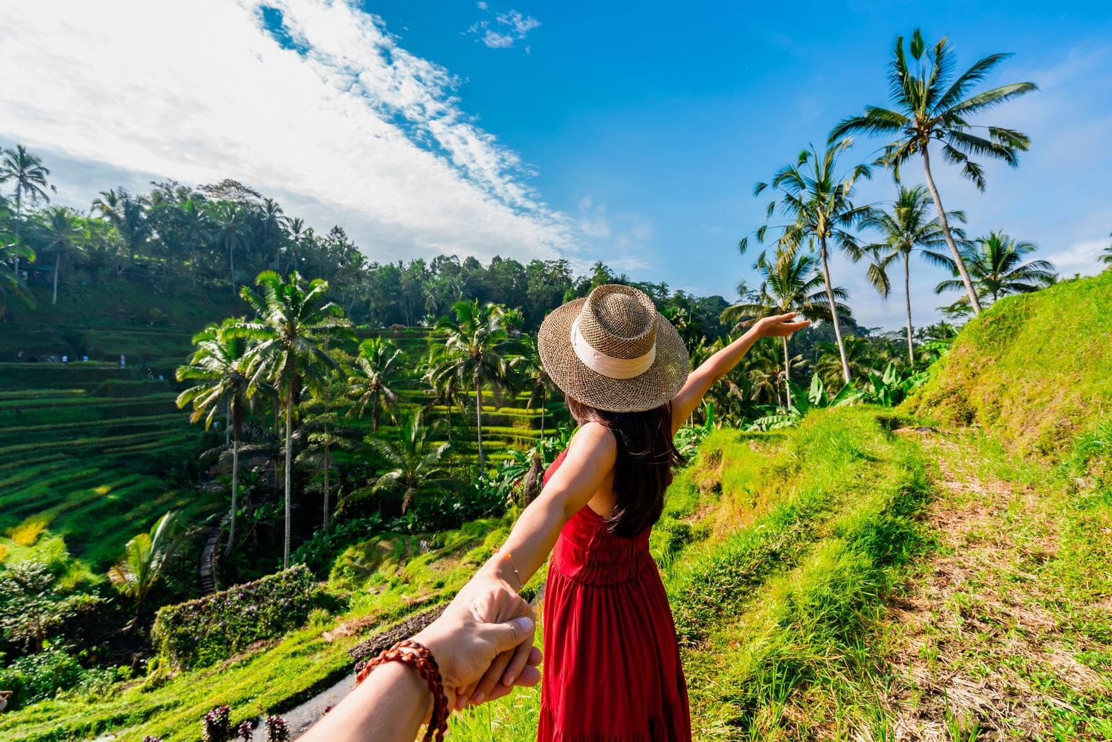 Frau in rotem Kleid vor Reisterrassen mit Palmen unter blauem Himmel in Bali, Indonesien.