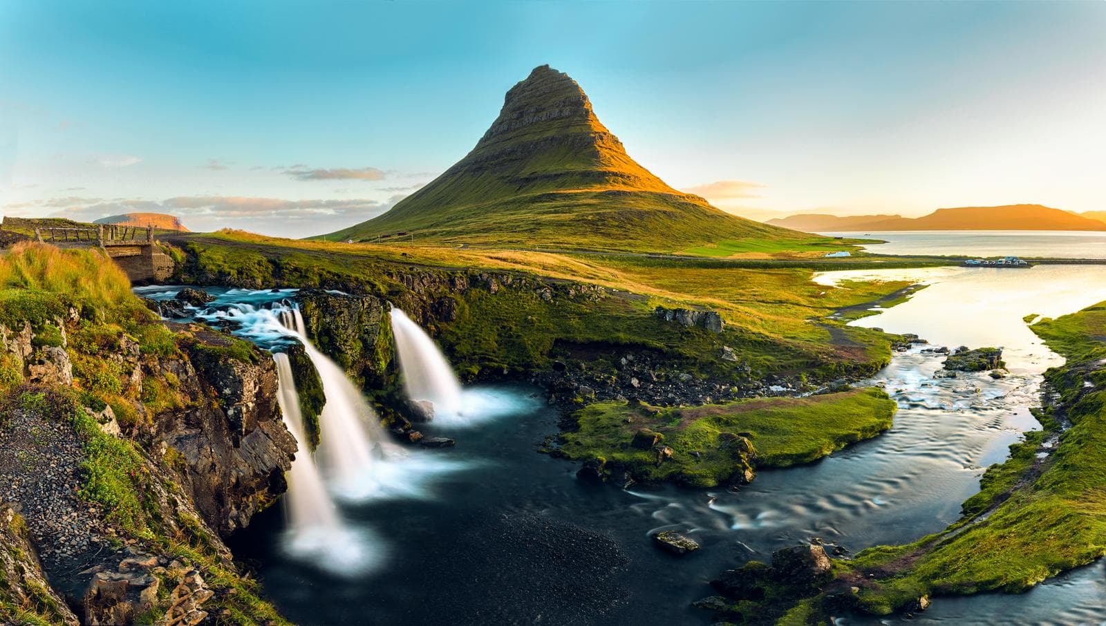 Island, Kirkjufell, grüner Berg bei Sonnenuntergang mit Wasserfall und Fluss.