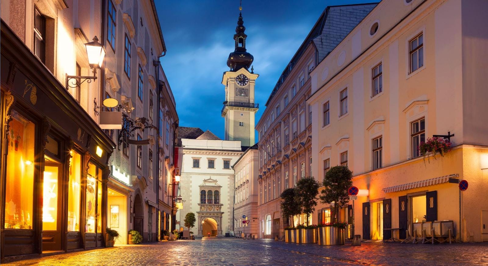 Pflastergasse in Linz, Österreich, mit historischem Stadttor im Abendlicht.