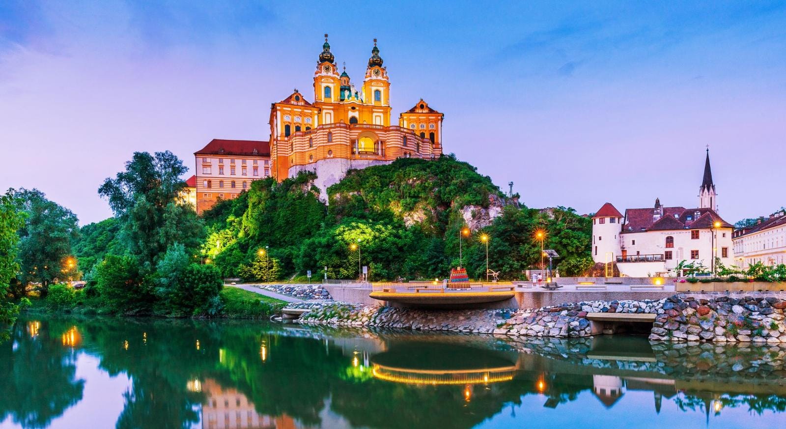 Barockes Stift Melk in Österreich, auf grünem Hügel über spiegelndem Fluss.