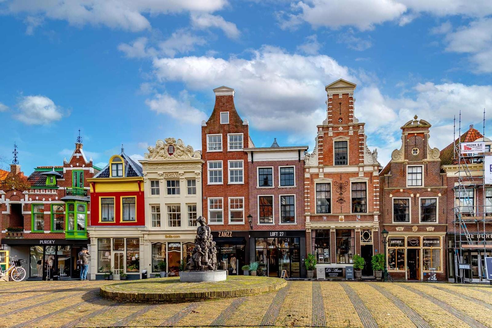 Bunte Giebelhäuser am Platz in Alkmaar, Niederlande, blauem Himmel, Statue im Vordergrund.