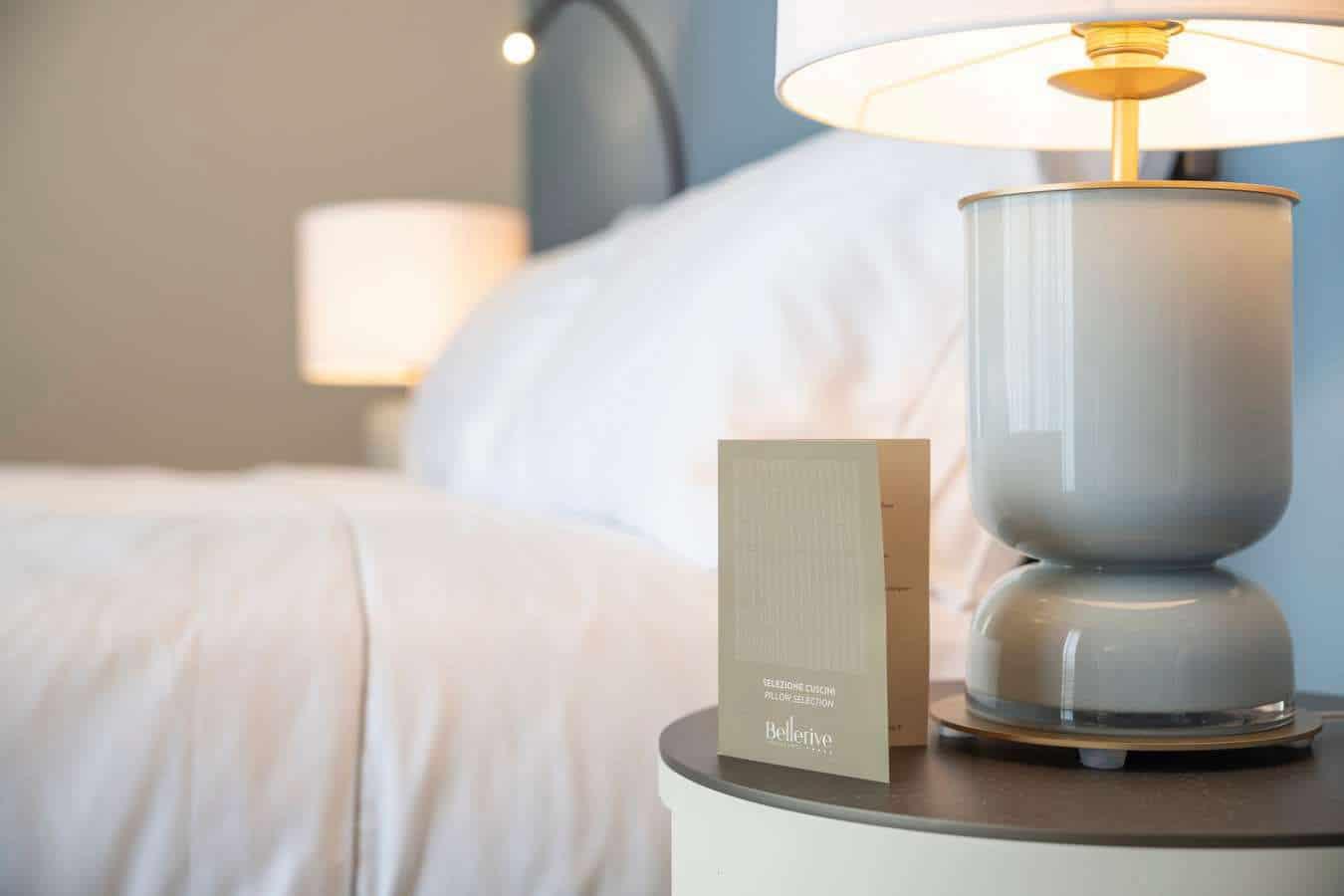 Elegantes Hotelzimmer mit grauer Lampe, weißer Bettwäsche und modernem Nachtisch.