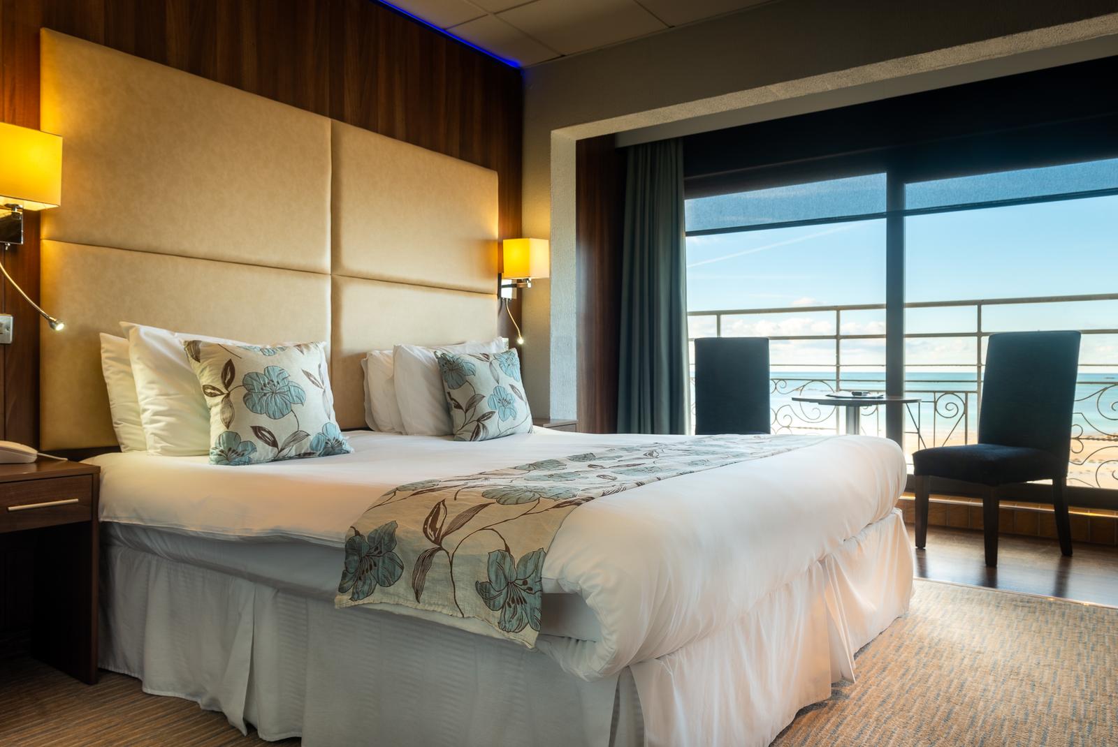 Modernes Hotelzimmer mit Meerblick, großem Bett, Blumenmuster und gemütlicher Beleuchtung.