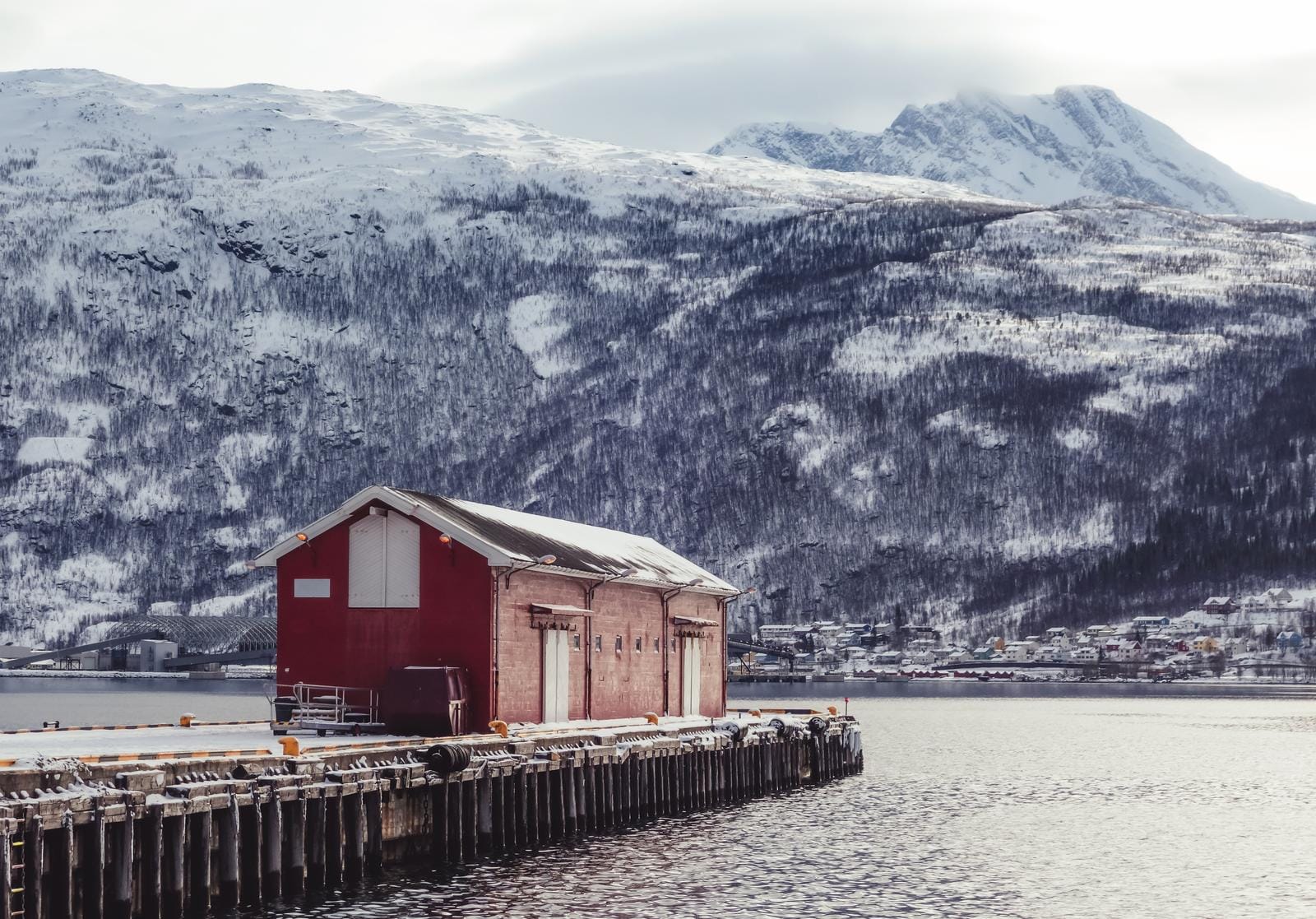 Rotes Lagerhaus am verschneiten Fjord, Norwegen; ruhige Winterlandschaft.