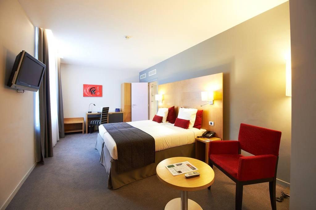 Modernes Hotelzimmer mit Doppelbett, roten Akzenten, Schreibtisch und Flachbildfernseher.