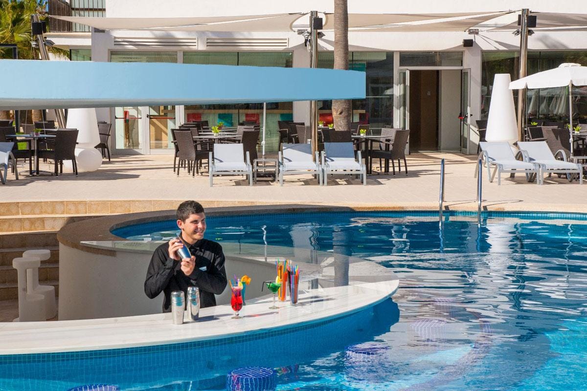 Swim-up-Bar am Pool mit Barkeeper, helles Ambiente, moderne Liegen, sonnig.