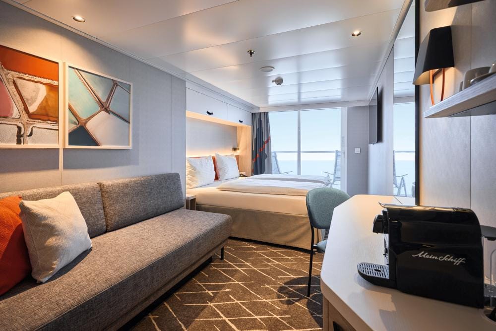 Modernes Hotelzimmer mit Balkon, grauer Couch, Kunst an der Wand und Kaffeemaschine.