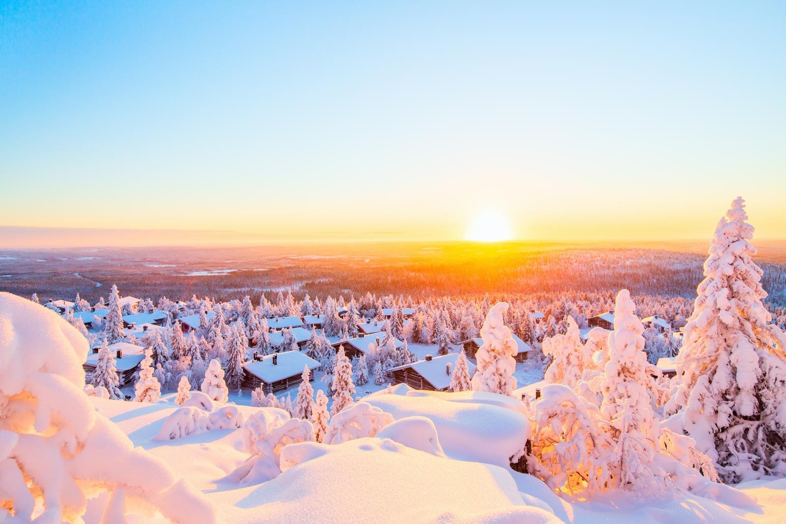 Verschneites finnisches Dorf im Sonnenuntergang mit schneebedeckten Tannenbäumen.