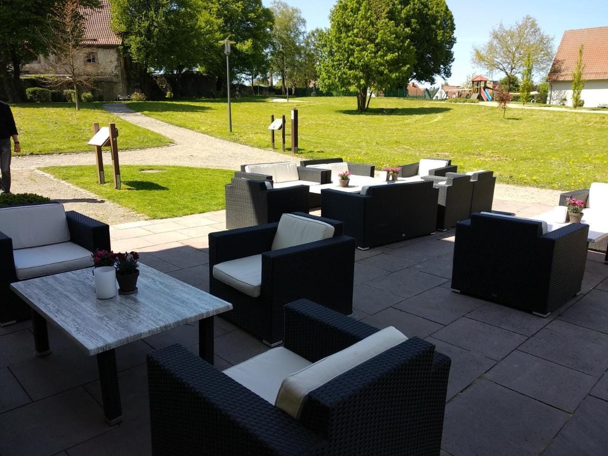 Hotelterrasse mit modernen schwarzen Rattanmöbeln, grüne Wiese und blauer Himmel.
