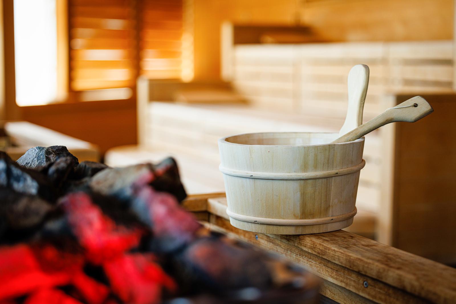 Sauna mit Holzinterieur, Eimer und Schöpfer am Holzgeländer, warme Lichtstimmung.