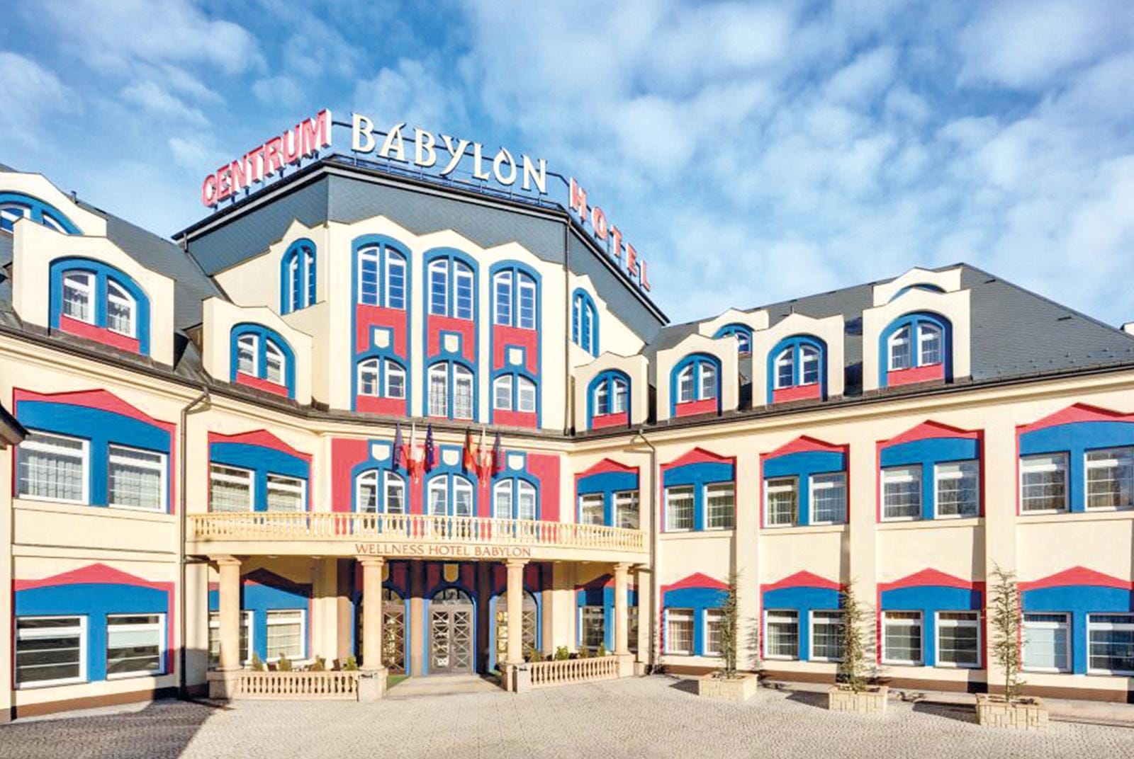 Buntes Hotelgebäude mit blauen und roten Akzenten, sonniges Wetter, einladende Fassade.