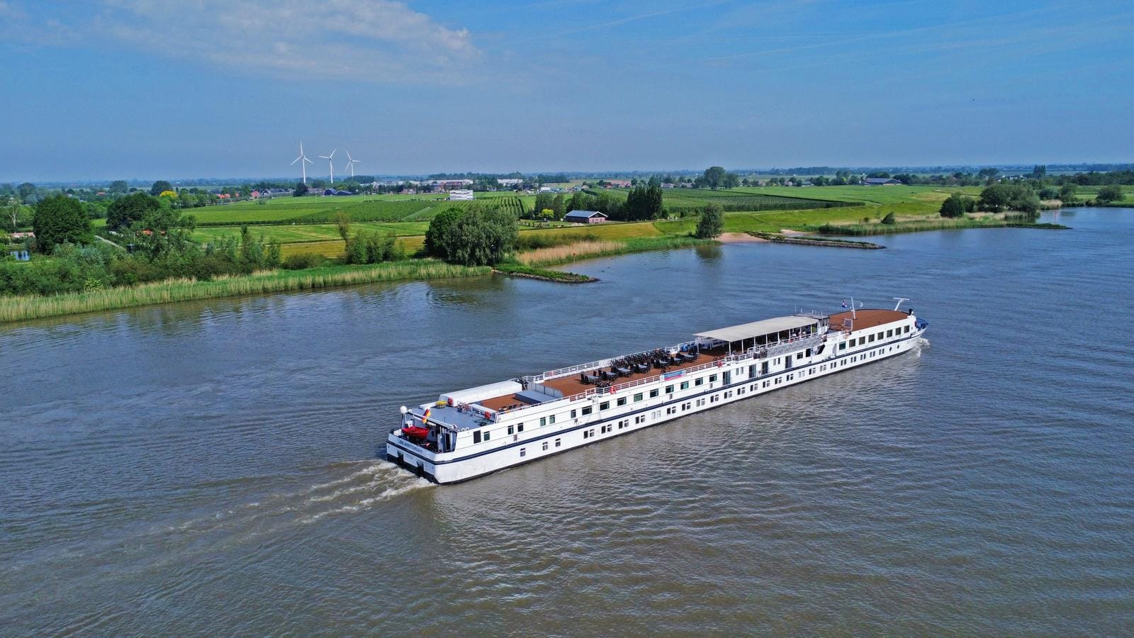 Flusskreuzfahrtschiff in den Niederlanden gleitet an grünen Landschaften und Windrädern vorbei.