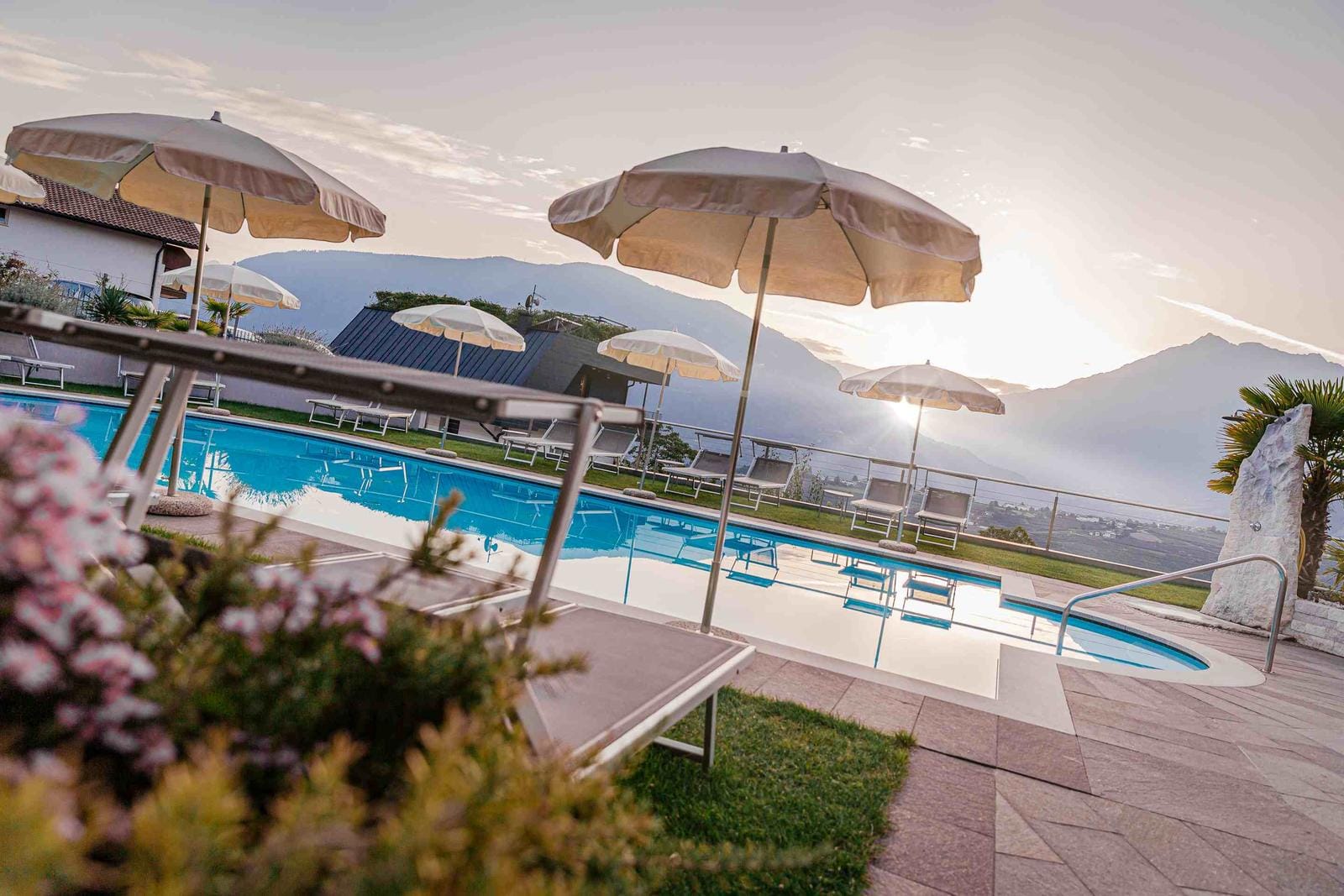 Hotelpool mit Liegen und Schirmen, umgeben von Bergen bei Sonnenuntergang.