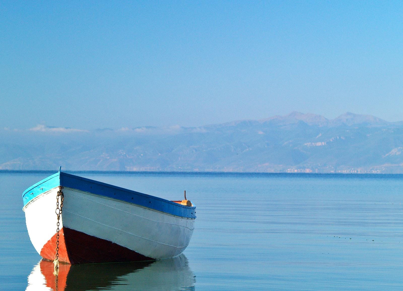 Kleines Boot auf ruhigem See mit Bergen im Hintergrund bei klarem Himmel.