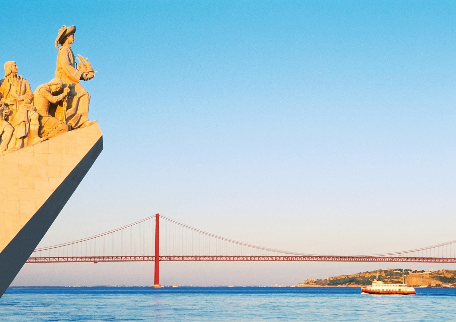 Skulpturen am Fluss mit roter Brücke und blauem Himmel in Lissabon, Portugal.