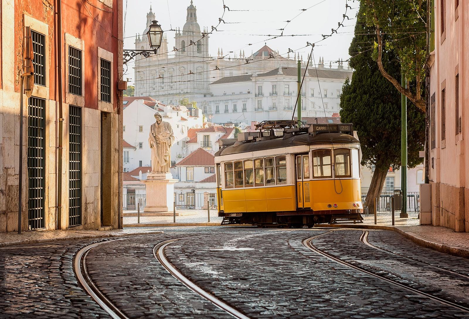Gelbe Tram in Lissabon, Portugal, vor pastellfarbenen Gebäuden und Statue.