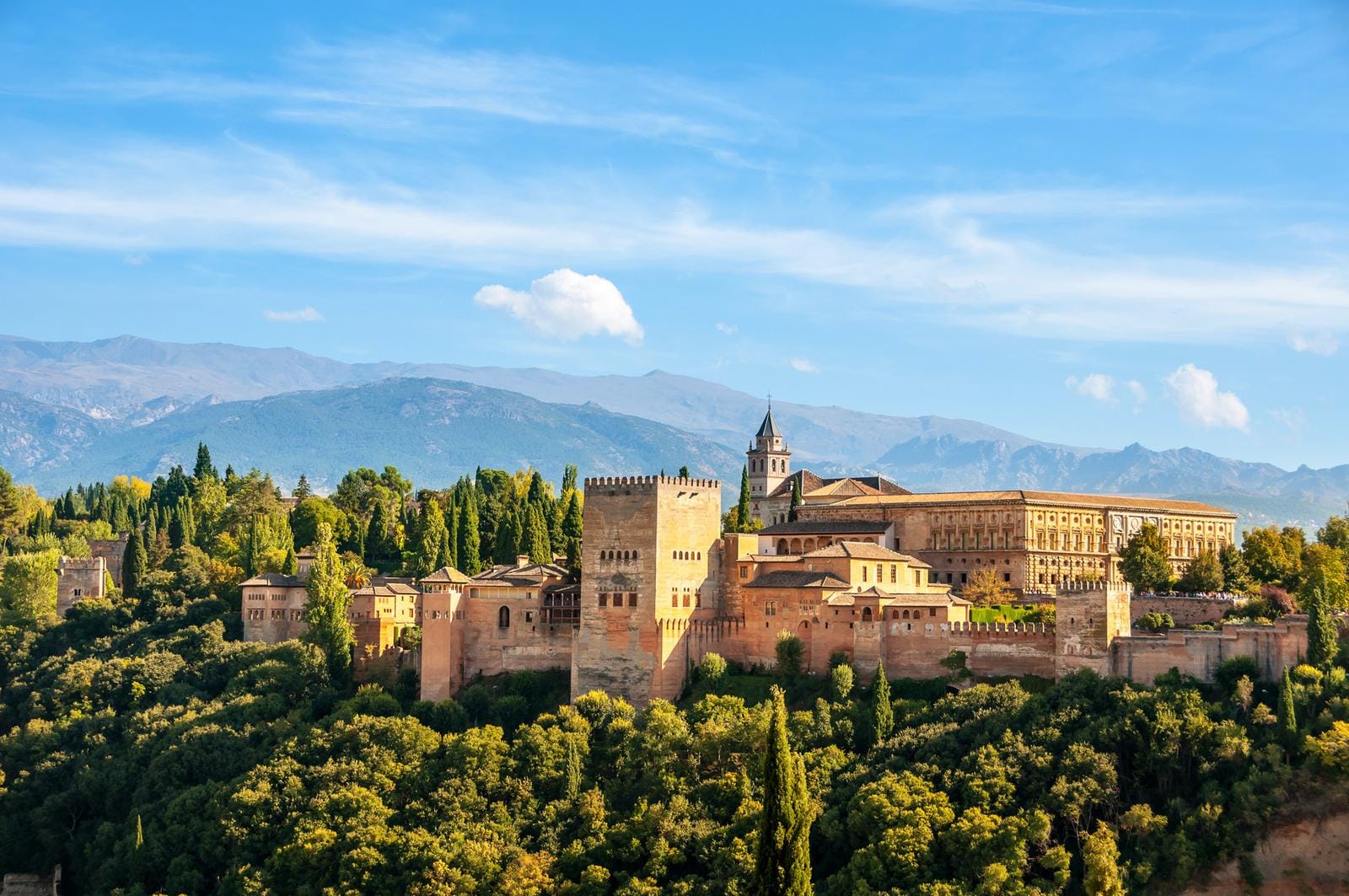 Alhambra in Granada, Spanien, vor bewaldeten Hügeln und blauem Himmel.