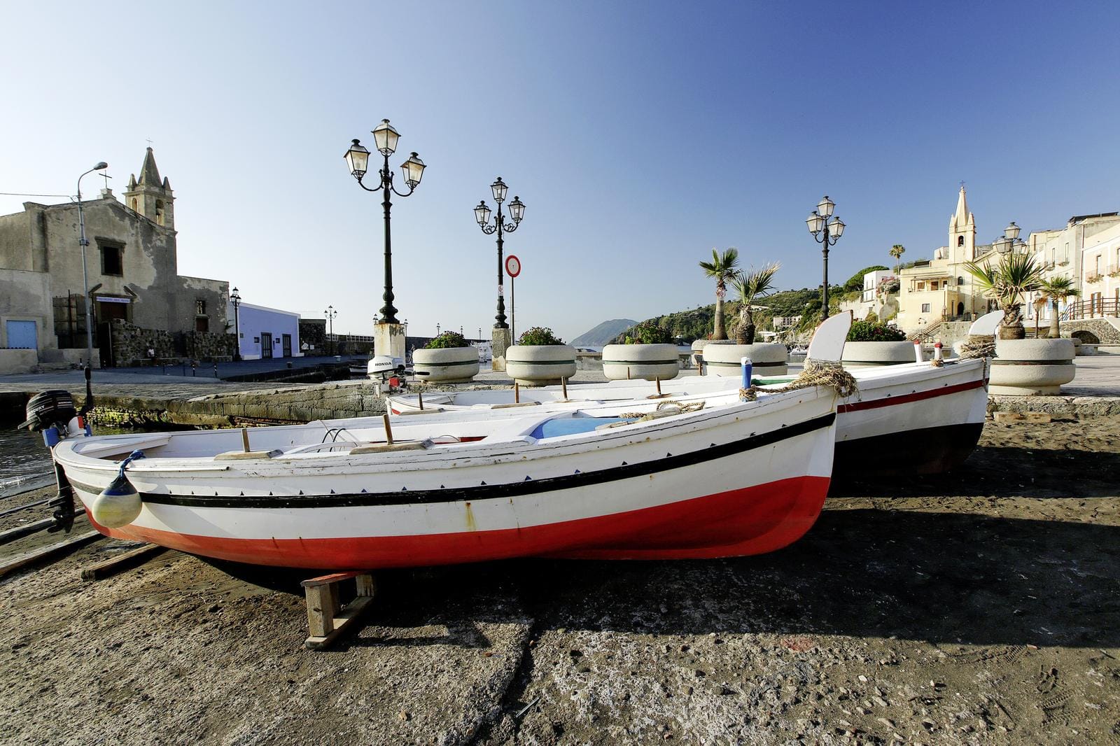 Bunte Boote am Ufer in Malfa, Sizilien, vor historischen Gebäuden und Laternen.