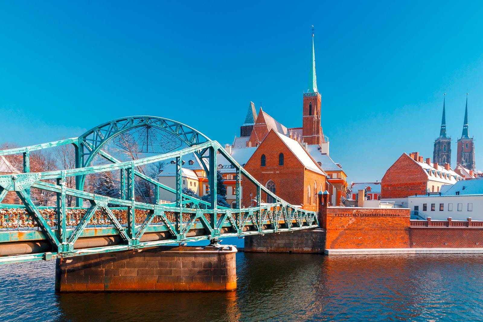 Türkisfarbene Brücke vor verschneiten, roten Backsteinkirchen in Breslau, Polen.