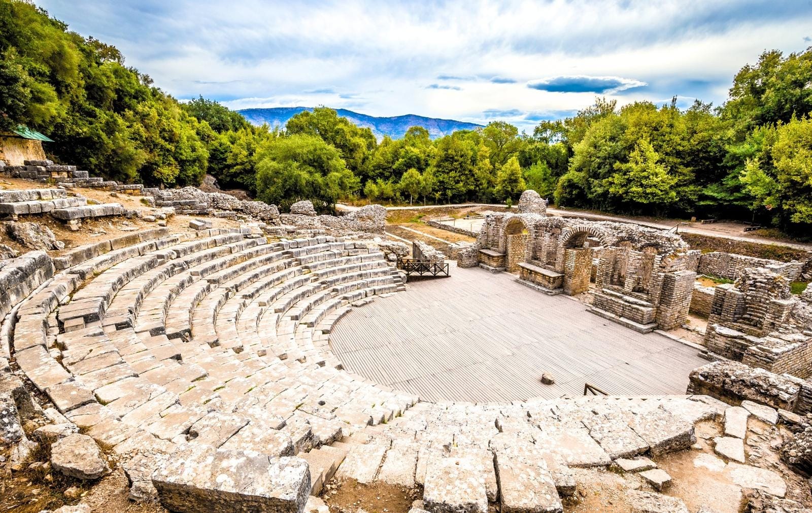 Antikes Theater in Albanien, umgeben von üppigem Wald und Bergen im Hintergrund.
