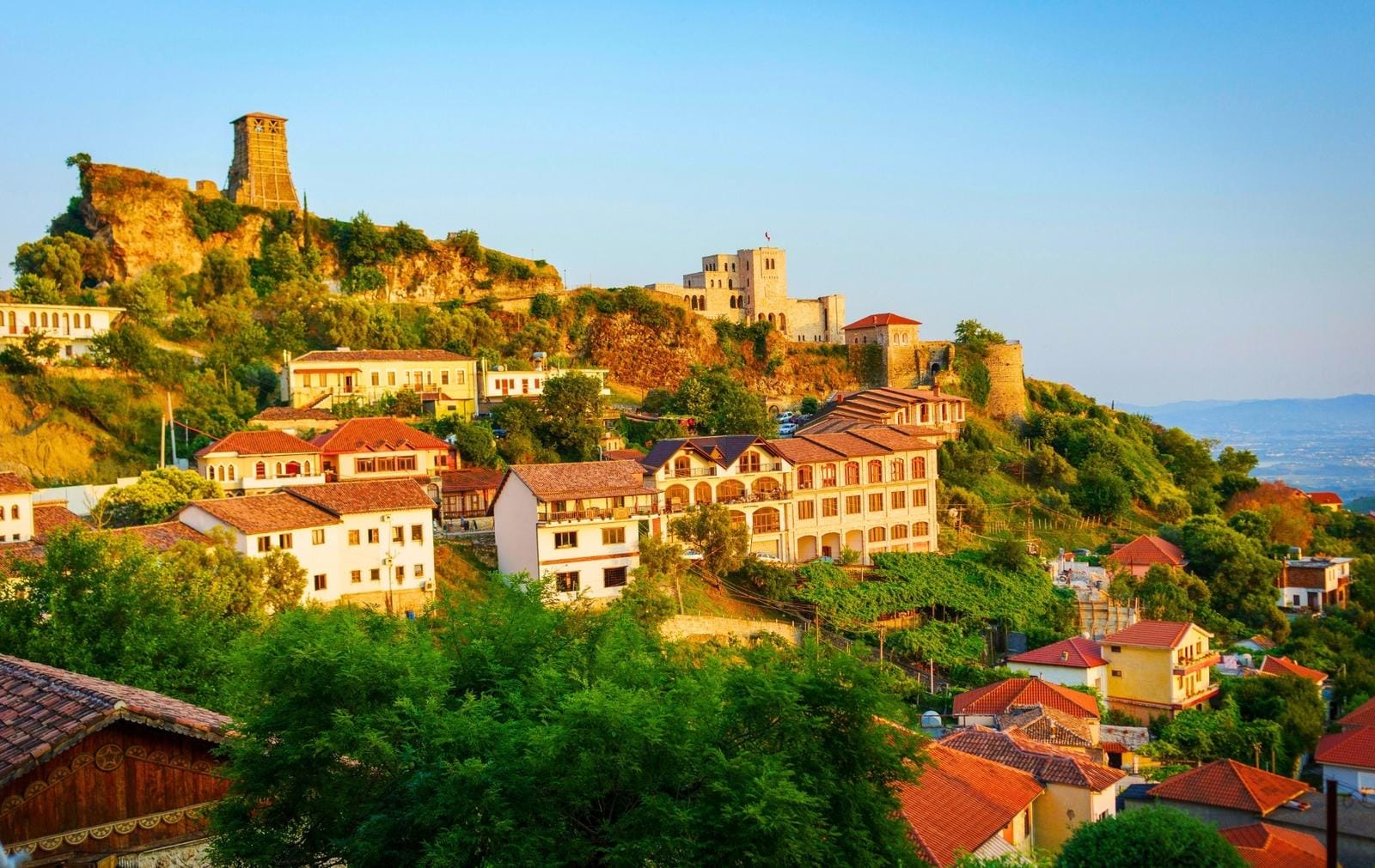 Stadt in Albanien mit Burg auf Hügel, umgeben von mediterraner Landschaft.