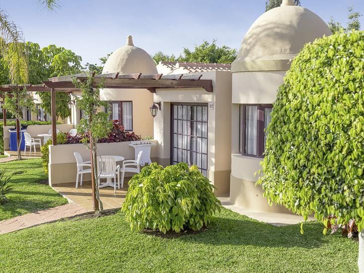 Mediterraner Bungalow mit Terrasse und Garten, helle Farben, ruhige Atmosphäre.
