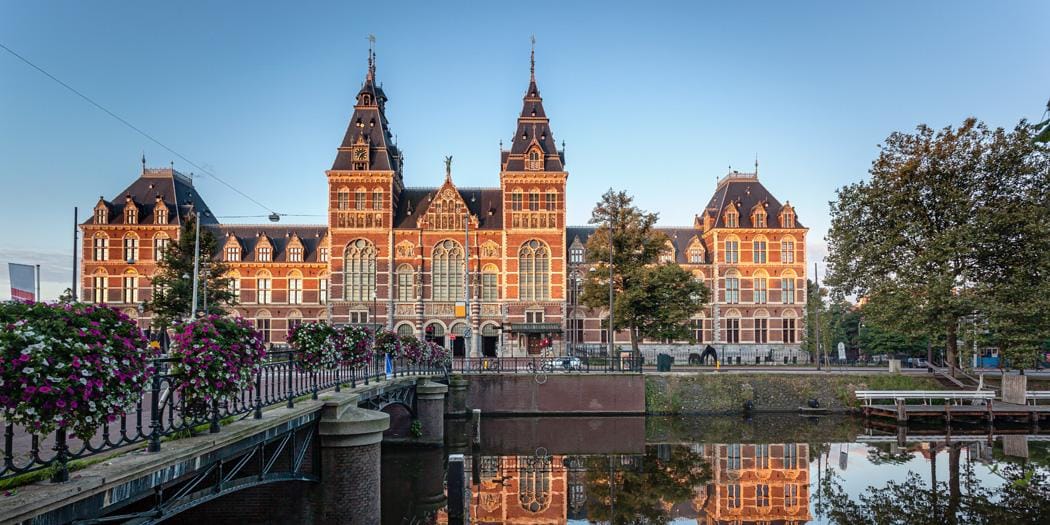 Backsteingebäude mit Türmen und Verspiegelung im Wasser, Amsterdam, Niederlande.
