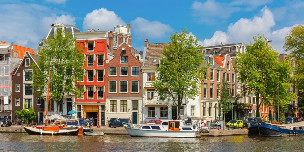 Bunte Grachtenhäuser und Boote am Kanal in Amsterdam bei sonnigem Wetter.