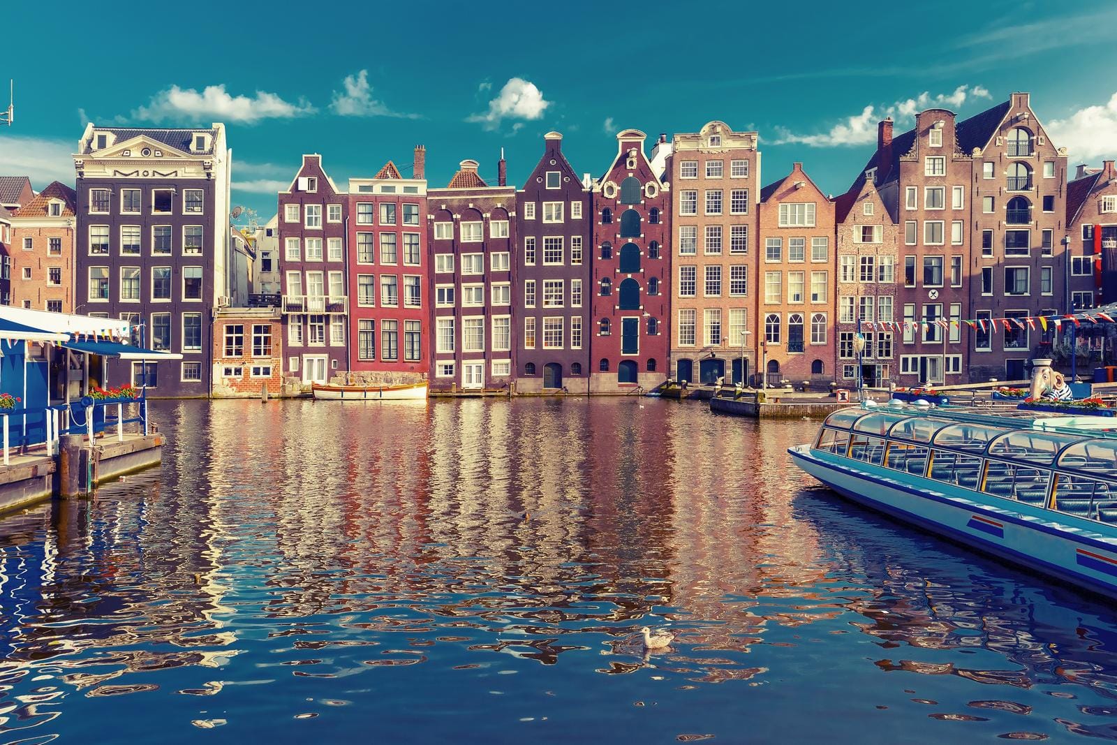 Bunte Grachtenhäuser am Wasser in Amsterdam, Niederlande, bei klarem Himmel.