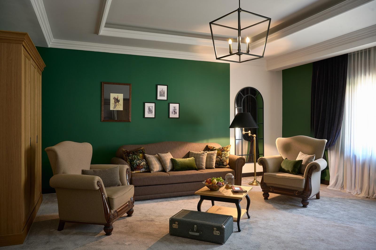 Elegantes Hotelzimmer mit klassischen Sesseln, grüner Wand und gemütlicher Beleuchtung.