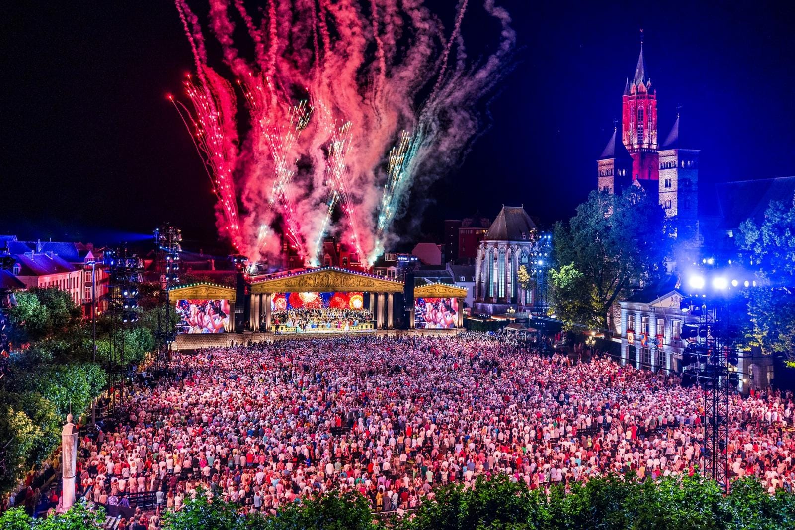 Andre Rieu in Maastricht mit buntem Feuerwerk und großer Menschenmenge vor historischer Kulisse.