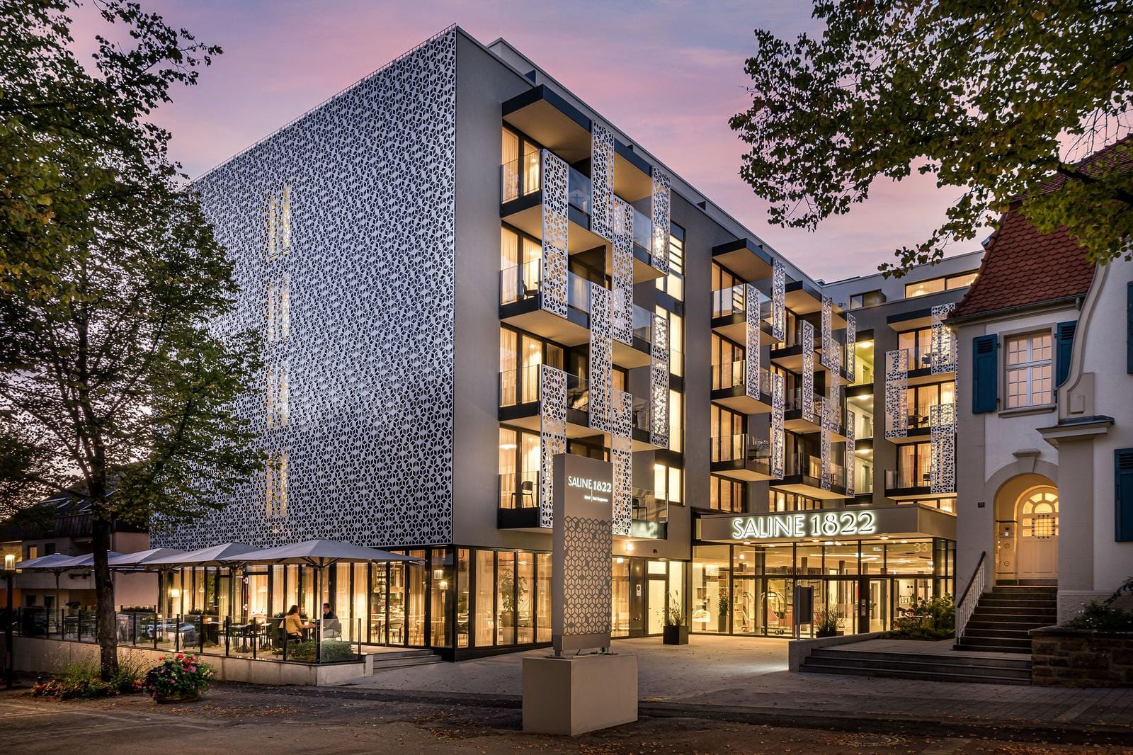 Moderne Hotelarchitektur mit beleuchteter Fassade und Außenterrasse bei Dämmerung.