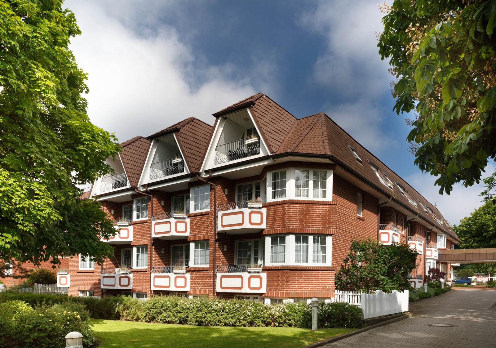 Rotes Backsteinhotel mit Satteldach, umgeben von grünen Bäumen und gepflegtem Garten.