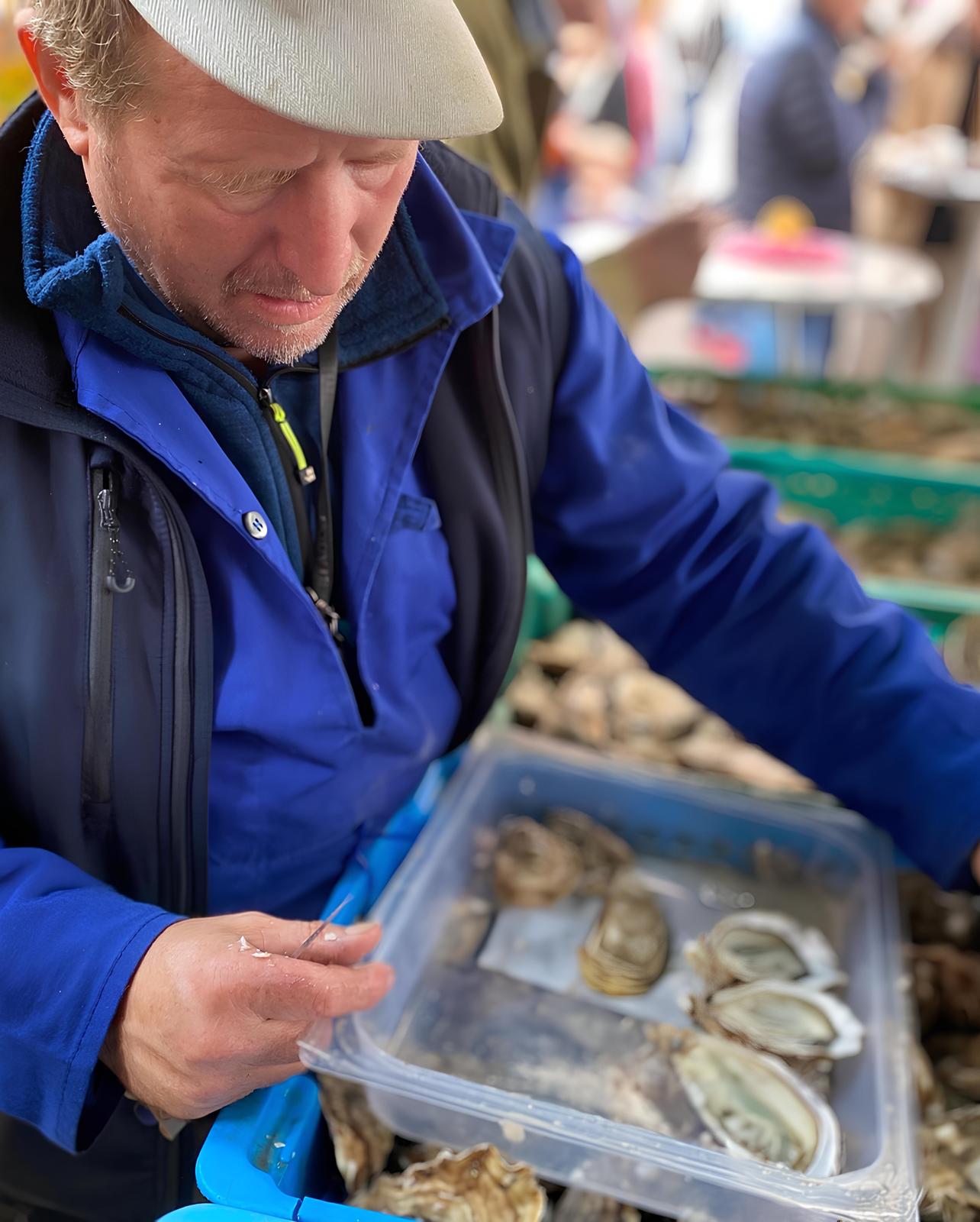 Mann in blauer Jacke verkauft Austern auf einem Markt.