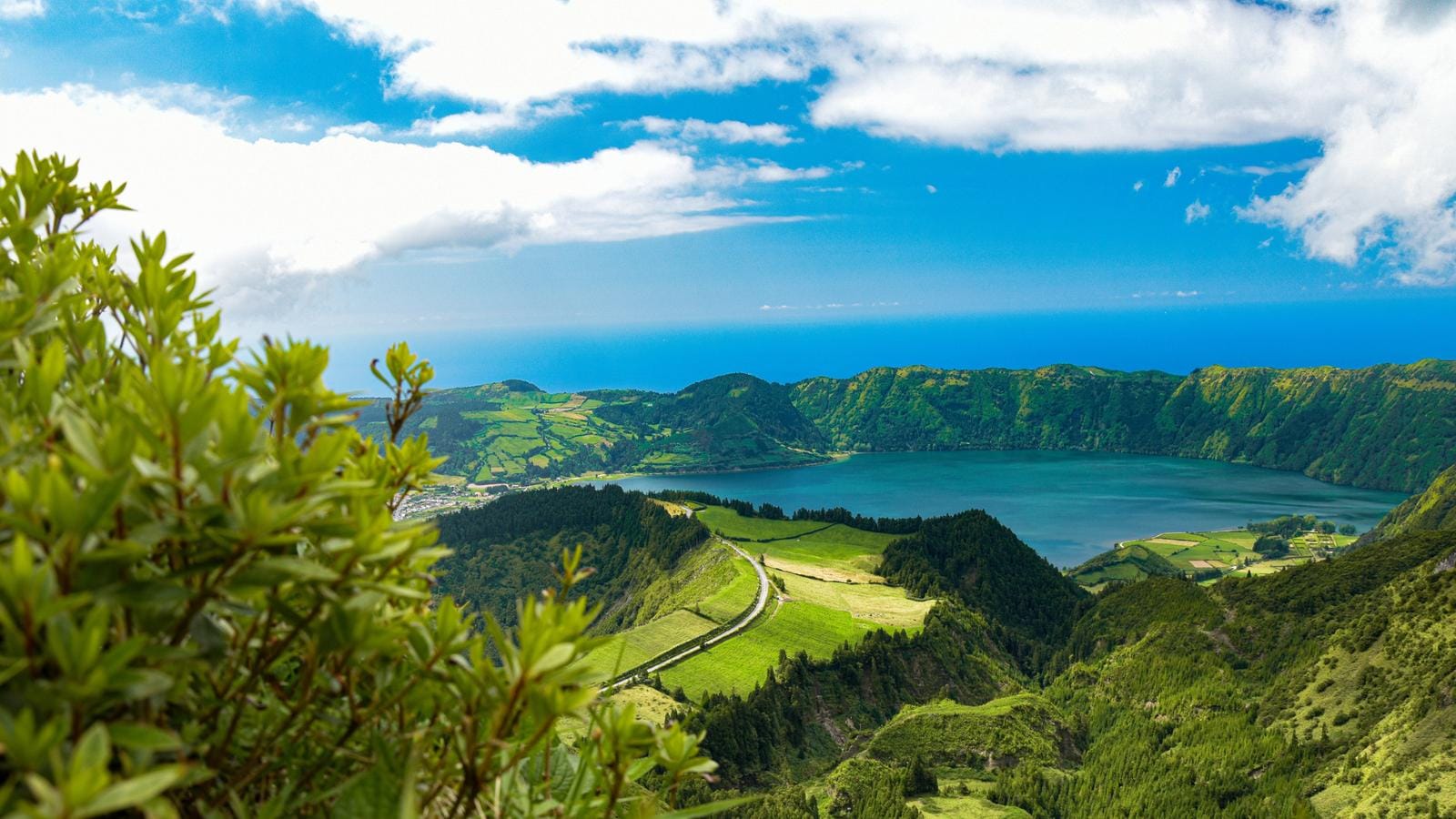 Grüne Landschaft und Kratersee auf São Miguel, Azoren, unter blauem Himmel.