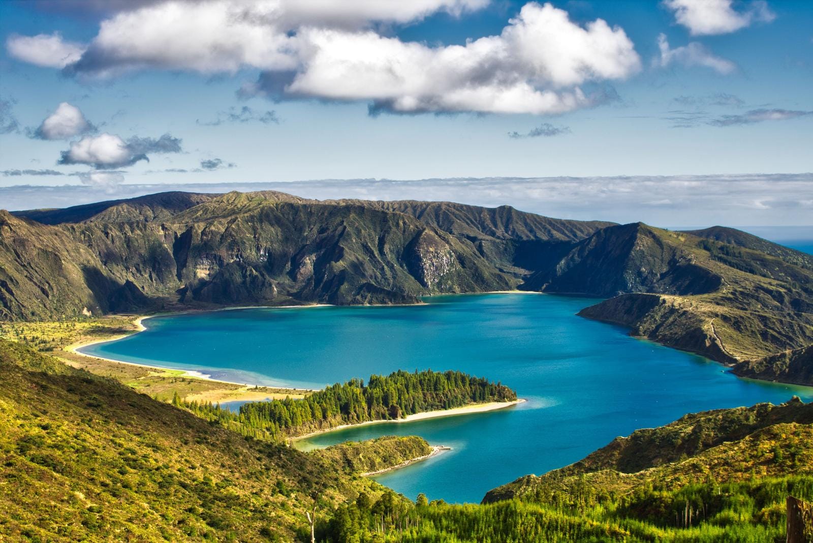Azoren, Portugal: Smaragdgrüner Kratersee umgeben von bewaldeten Hügeln und blauem Himmel.