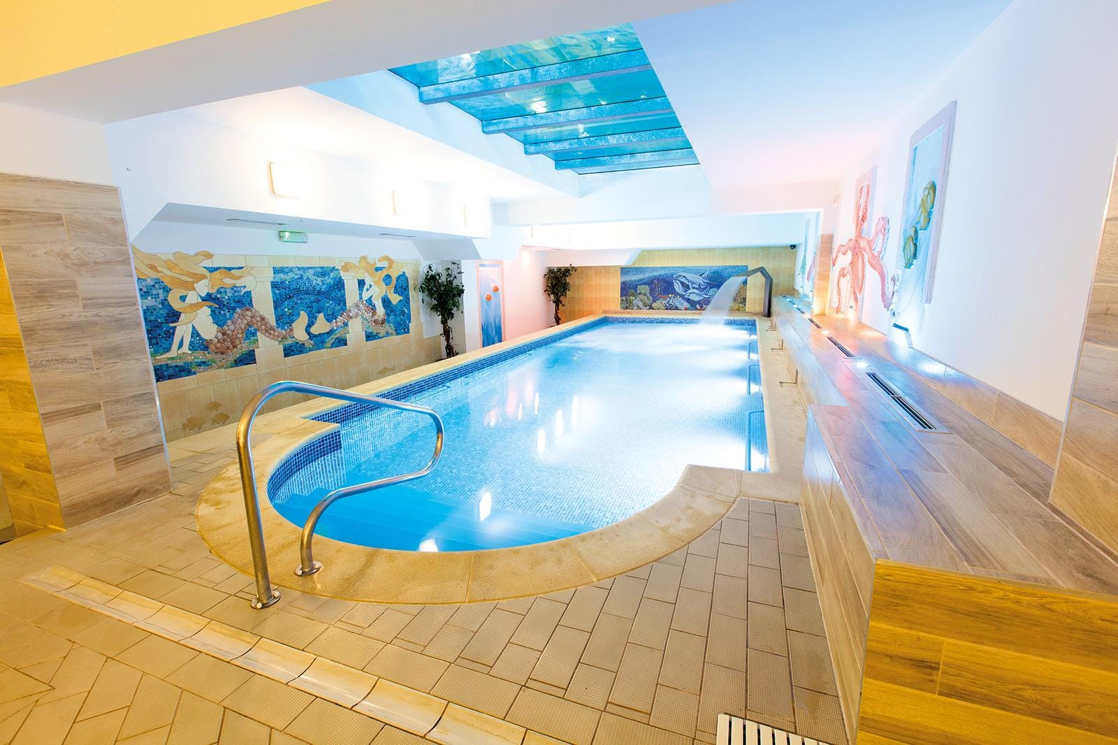 Helles Hallenbad mit Blauer Fliesen, Mosaikwand und moderner Beleuchtung.