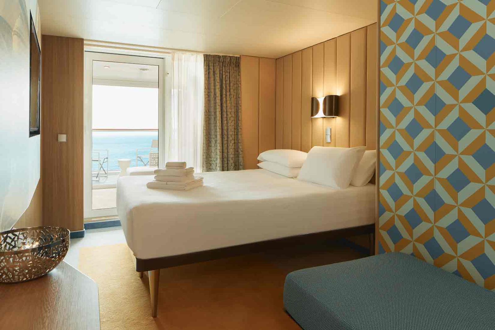 Modernes Hotelzimmer mit Meerblick, hellem Holz, geometrischer Tapete und Balkon.