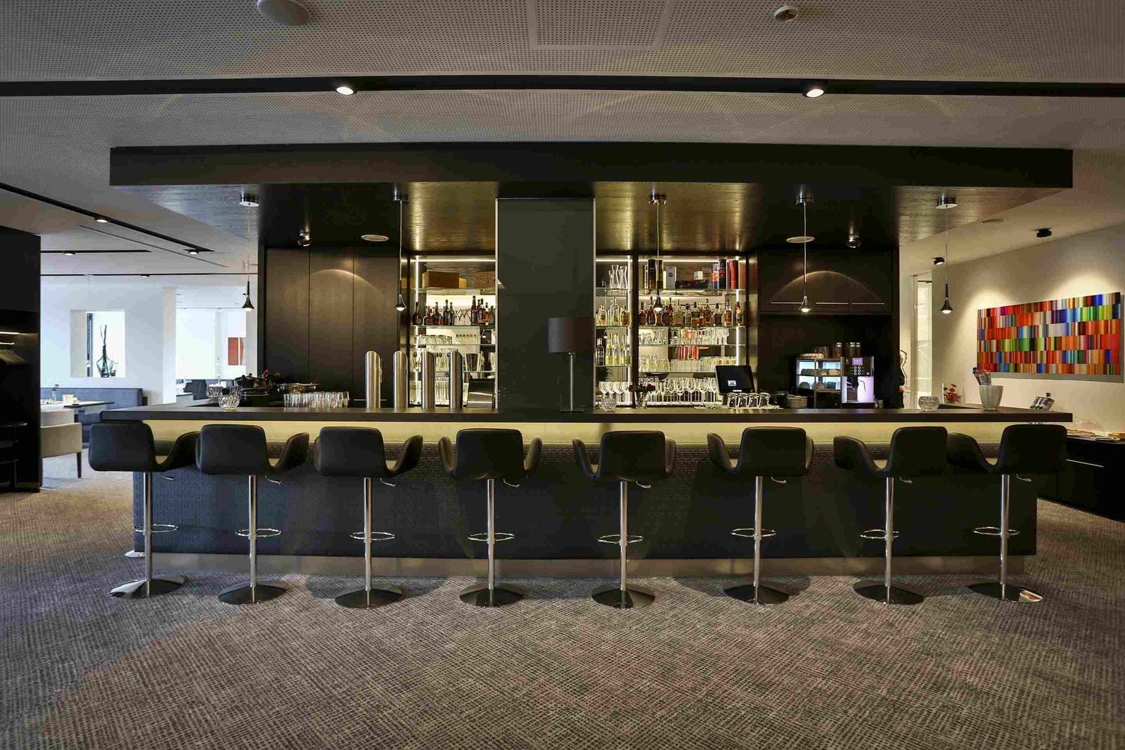 Moderne Hotelbar mit schwarzen Hockern, elegantem Design und beleuchteten Regalen.